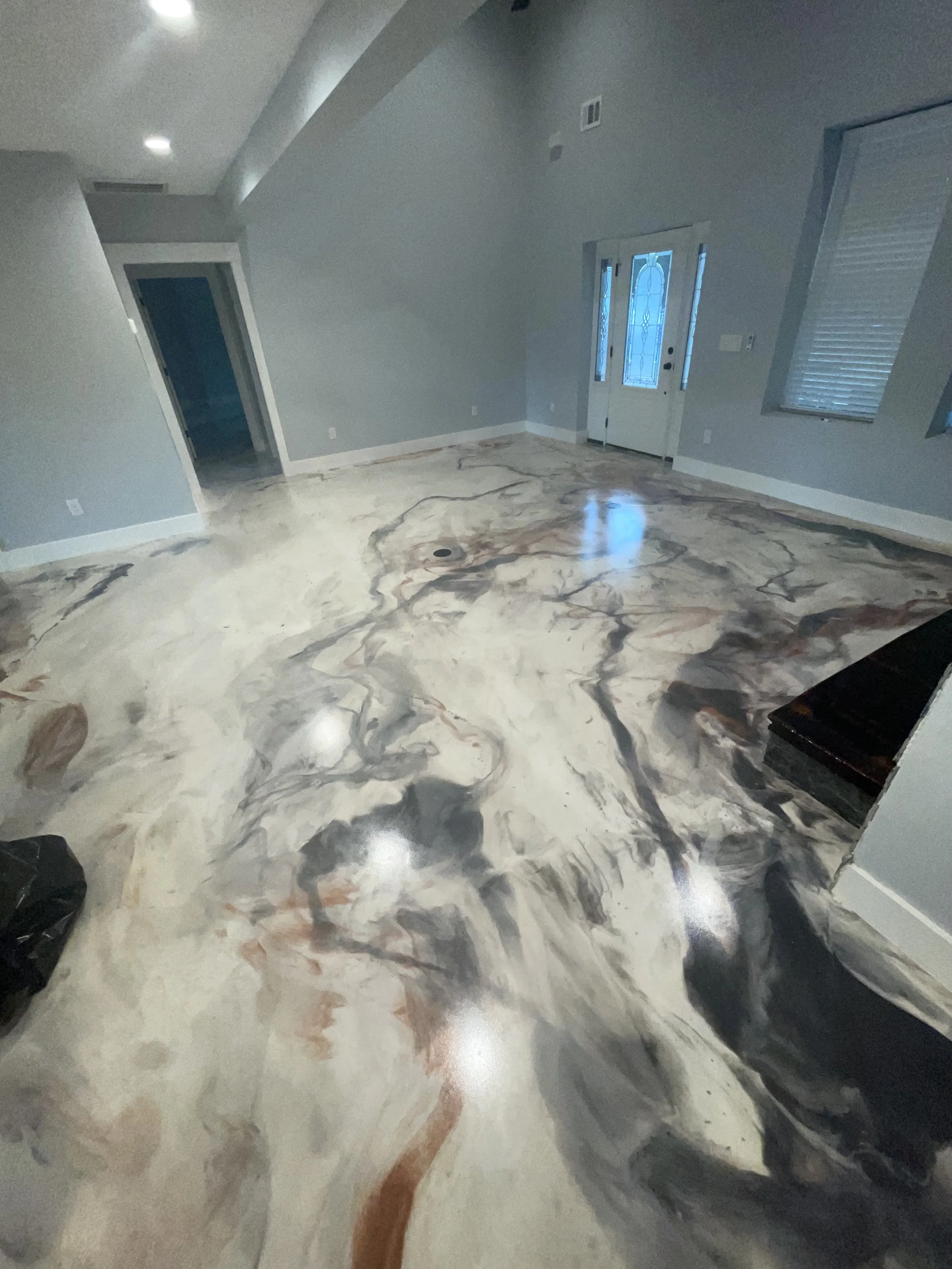 Empty living room with marble floor, gray walls, a ceiling with recessed lighting, and windows with blinds. Front door visible in the background.