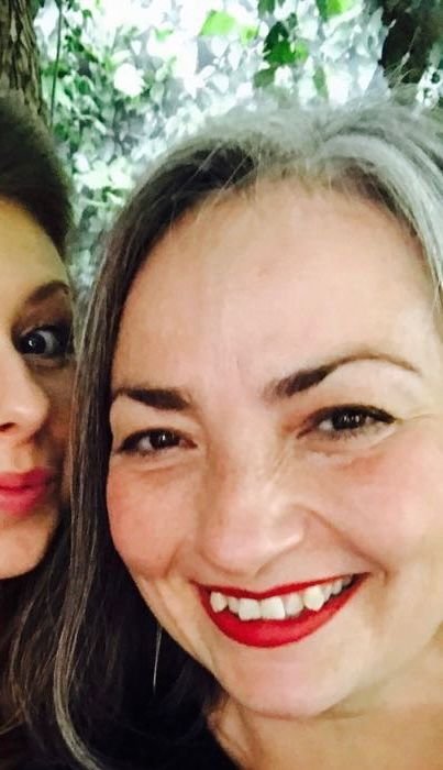 Nichol looking vibrant with big red lipstick on a big smile. You can see a bit of a friend in the selfie. Both smiling women. After her lung cancer treatment.