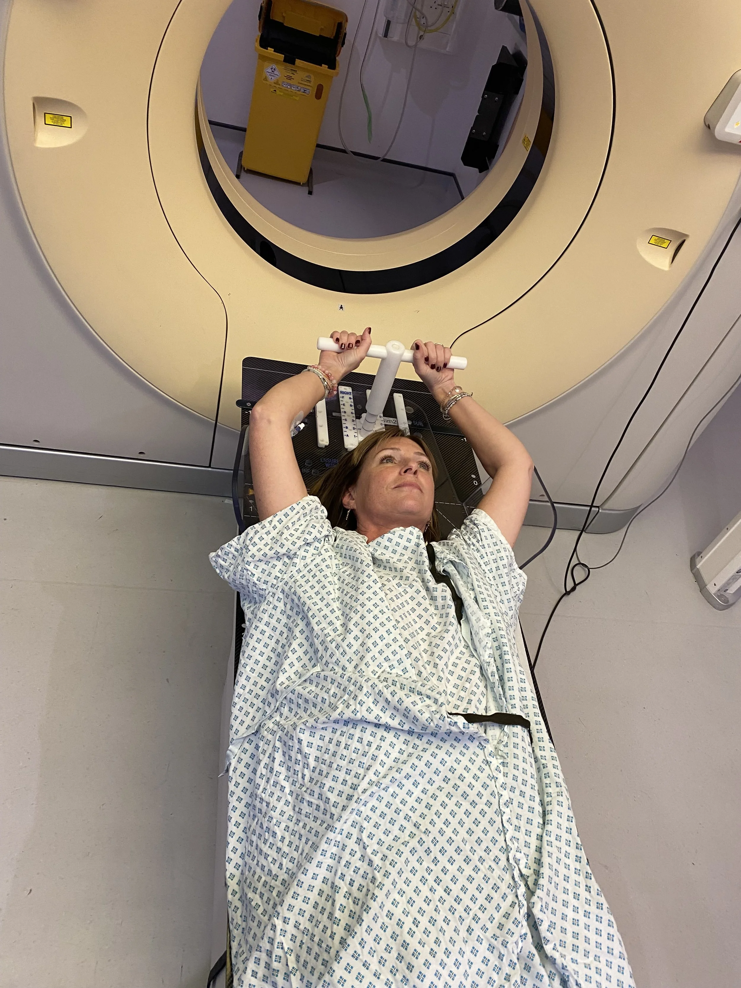 Natasha in a hospital gown, about to go into for radiation, holding her hands above her head on the bed