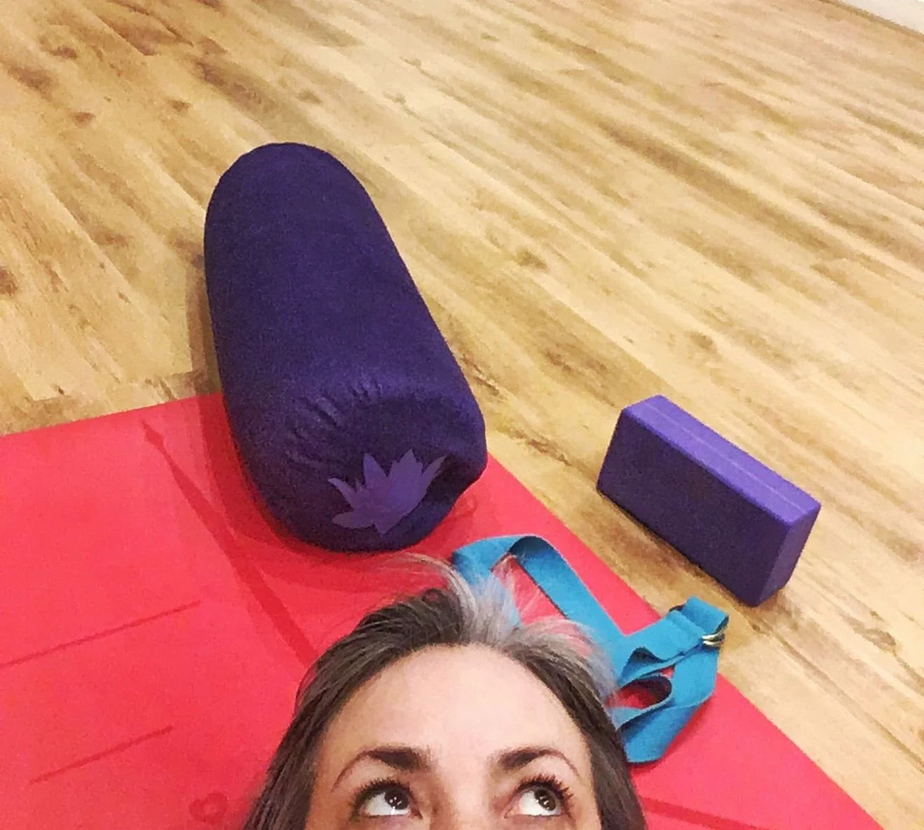 Somewhat humorous photo of Nichols eyes gazing up as she lays on a pilates mat and bolsters around her. Bright colours.