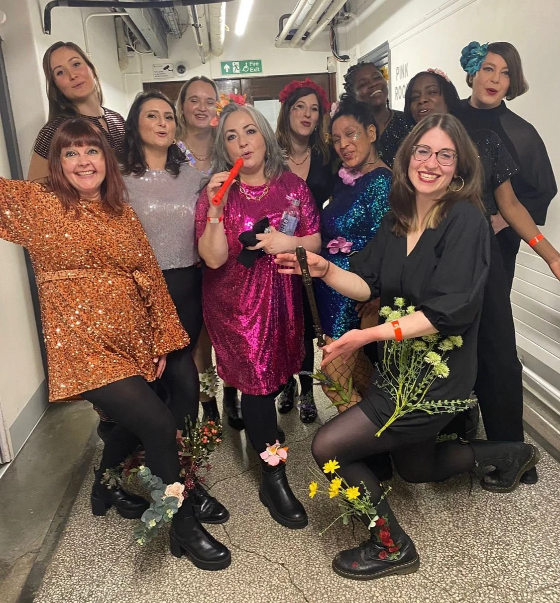 Nichol in the centre of a large group of young women, all dressed up in glittery cocktail dressed, with flowers around their shoes - all looking very happy and like they're having fun.. Yet Nichol has stage 4 lung cancer here.