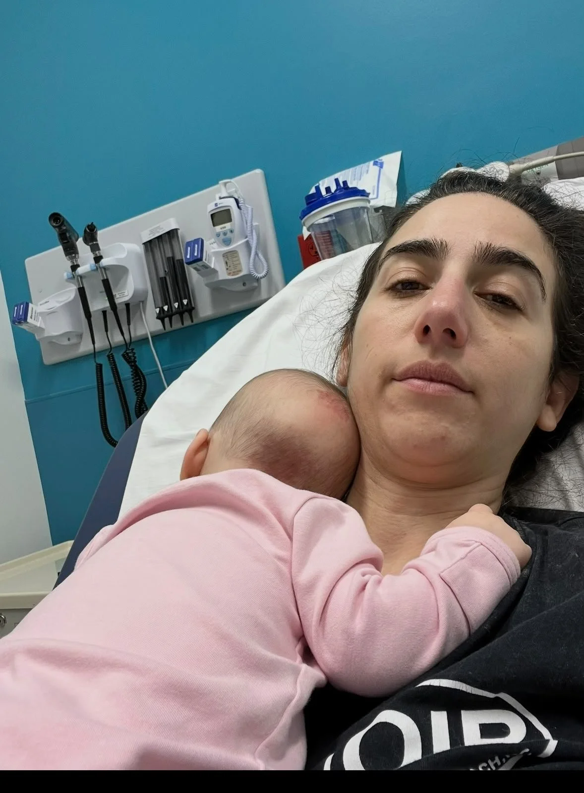 Mayya in a hospital bed, with an infant resting and sleeping across her chest