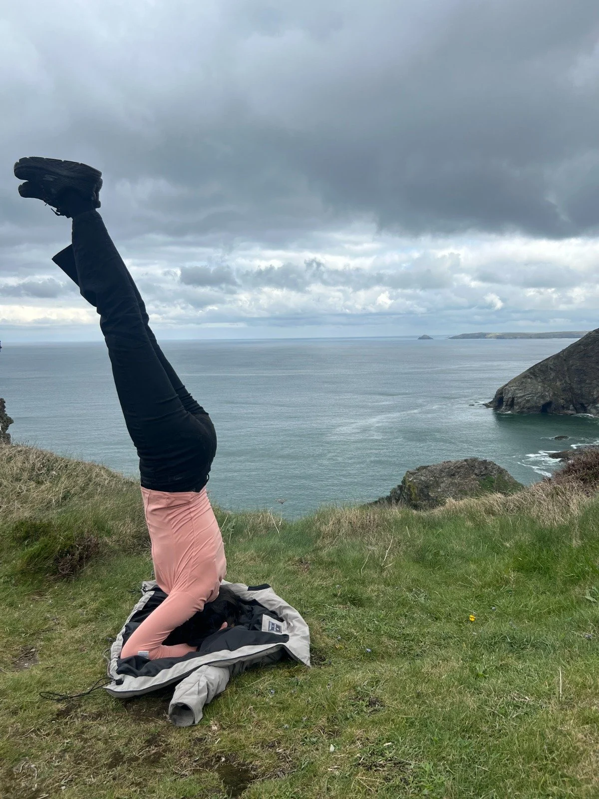 Rasika doing a handstand to show her health. On a grassy area with a beautiful sea background and blue and big clouds in the sky