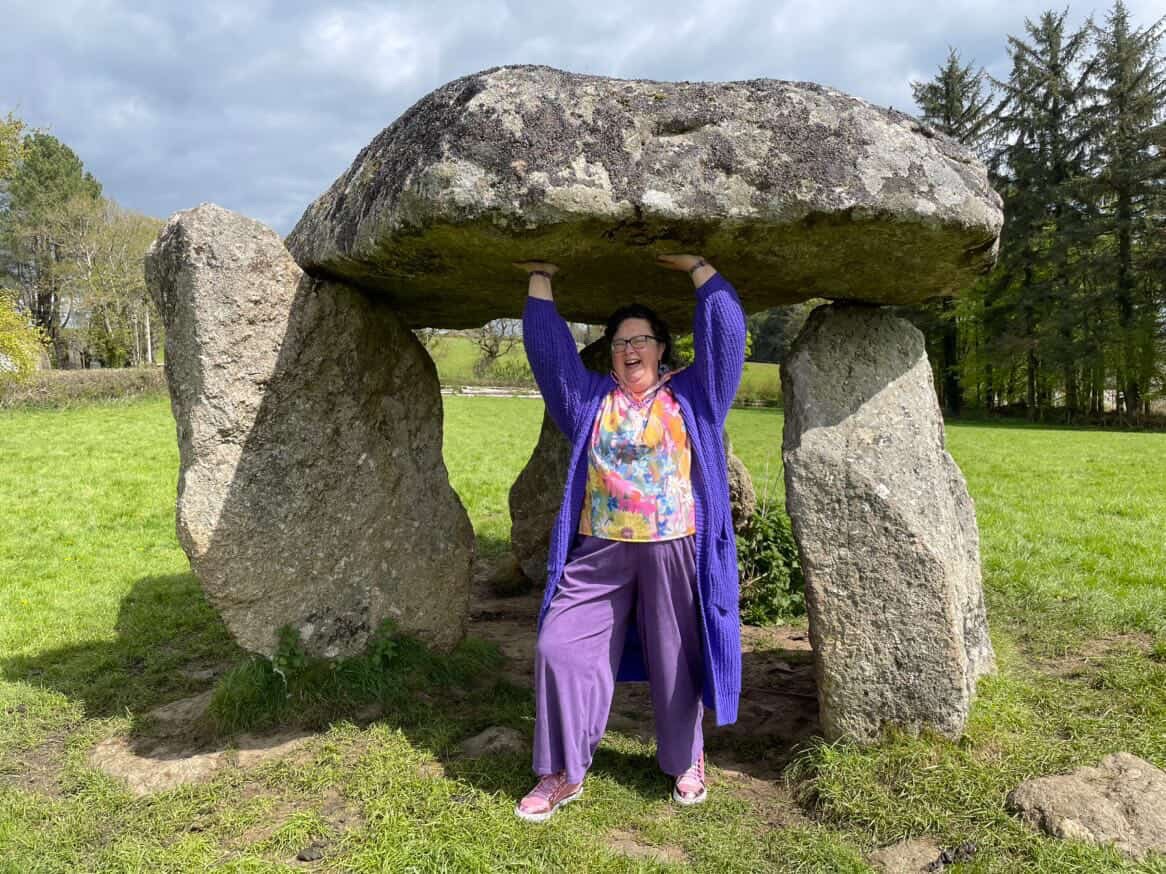 Allison, who has had 3 cancer diagnoses, holding up a boulder, wearing purple and laughing out loud.