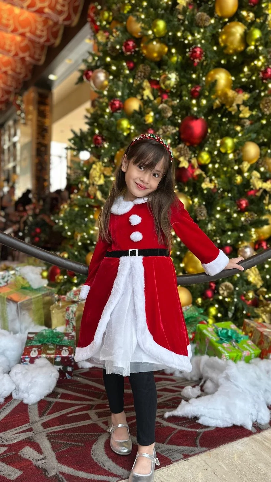 Kimberly's daughter in a Christmas dress in front of a Christmas tree - aged 5