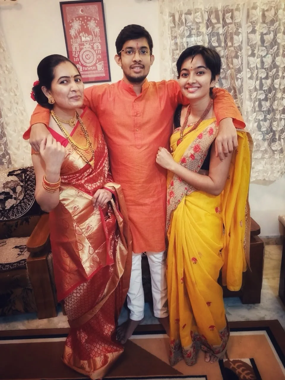 A young Rasika with her mother and family member in India. The two women wearing colourful saris and the young man in traditional dress.  Big smiles.