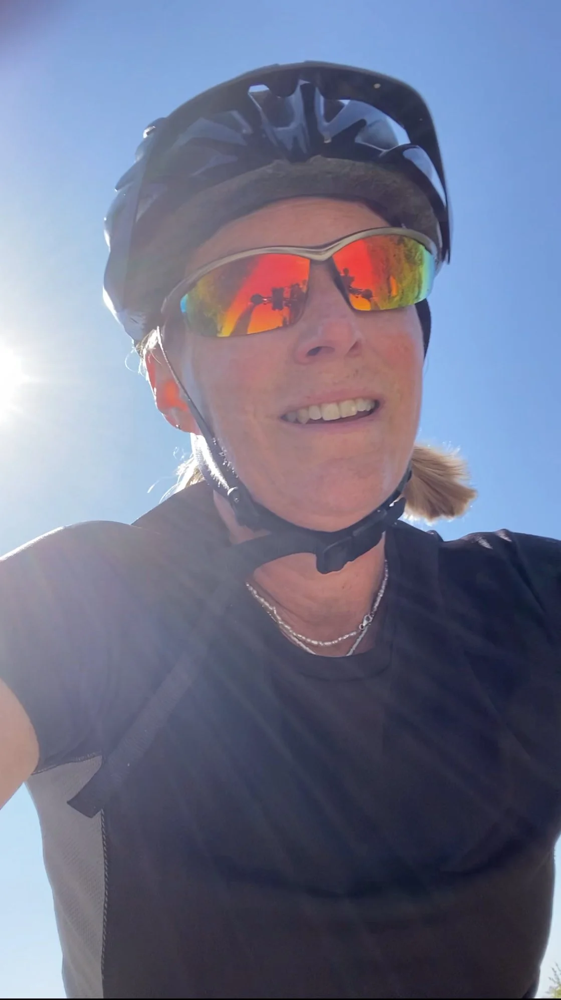 Close up of Natasha, with mirrored sun glasses and a strapped on helmet, clearly cycling.