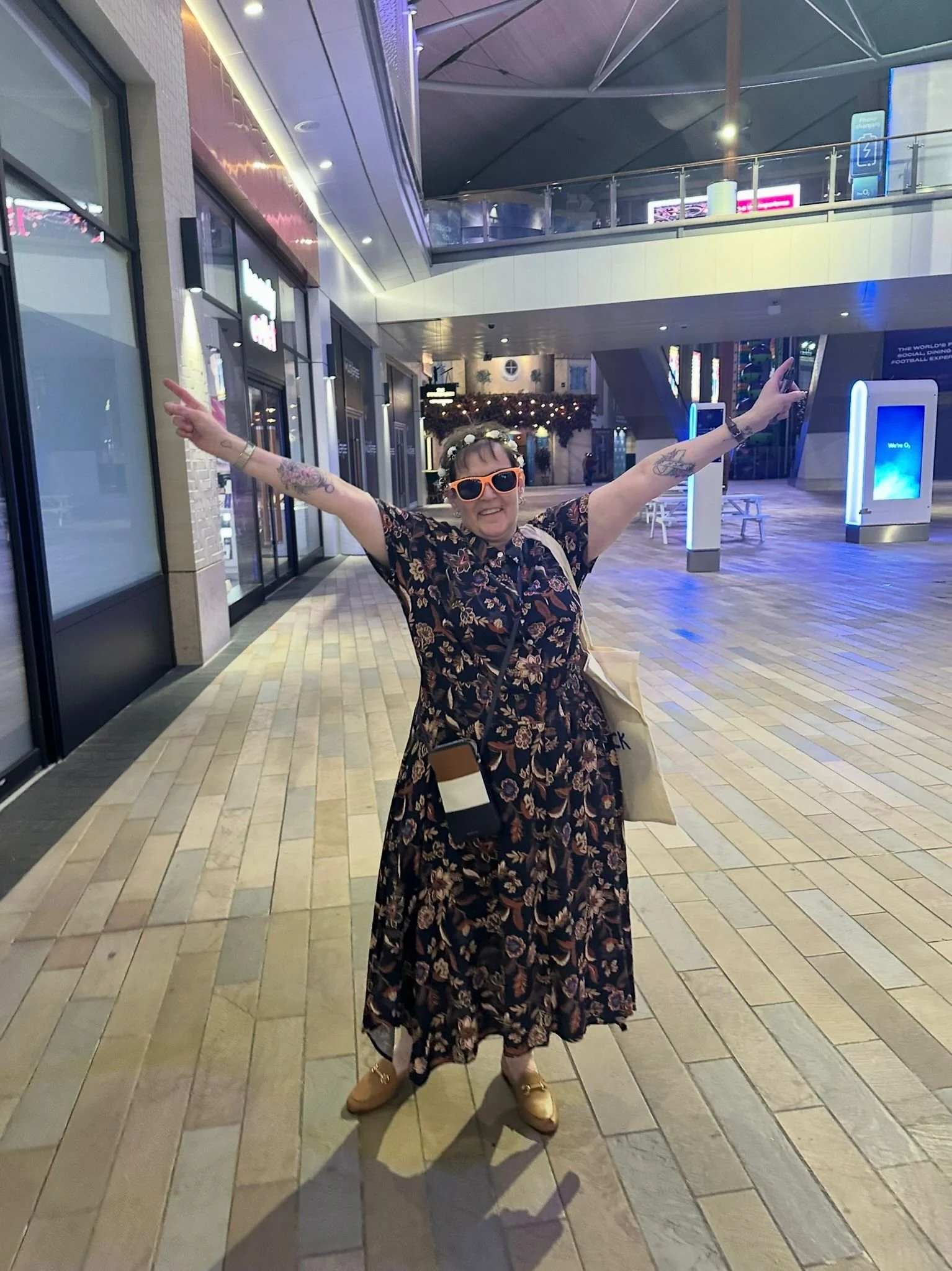 Julia wearing sun glasses and a dress with her hands up in the air as if celebrating.