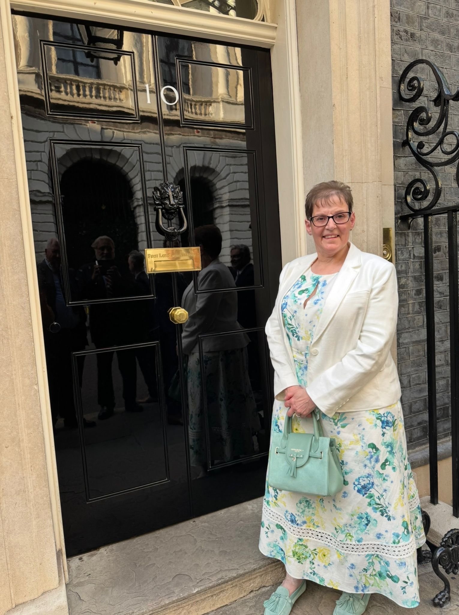 Joanne outside 10 Downing Street, to advocate for people living with lung cancer. She wears a long floral spring dress and a big smile outside the door