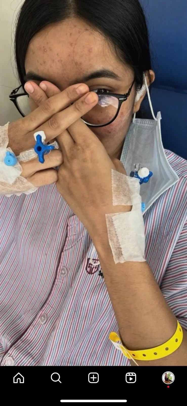 Photo showing Rasika hiding her face which is covered in rashes, she has several ports in her hands and arms, hospital bracelet.