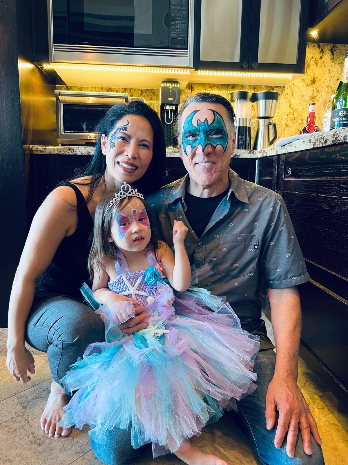 Kimberly with husband and young daughter - each with their faces painted and the daughter dressed like a princess.