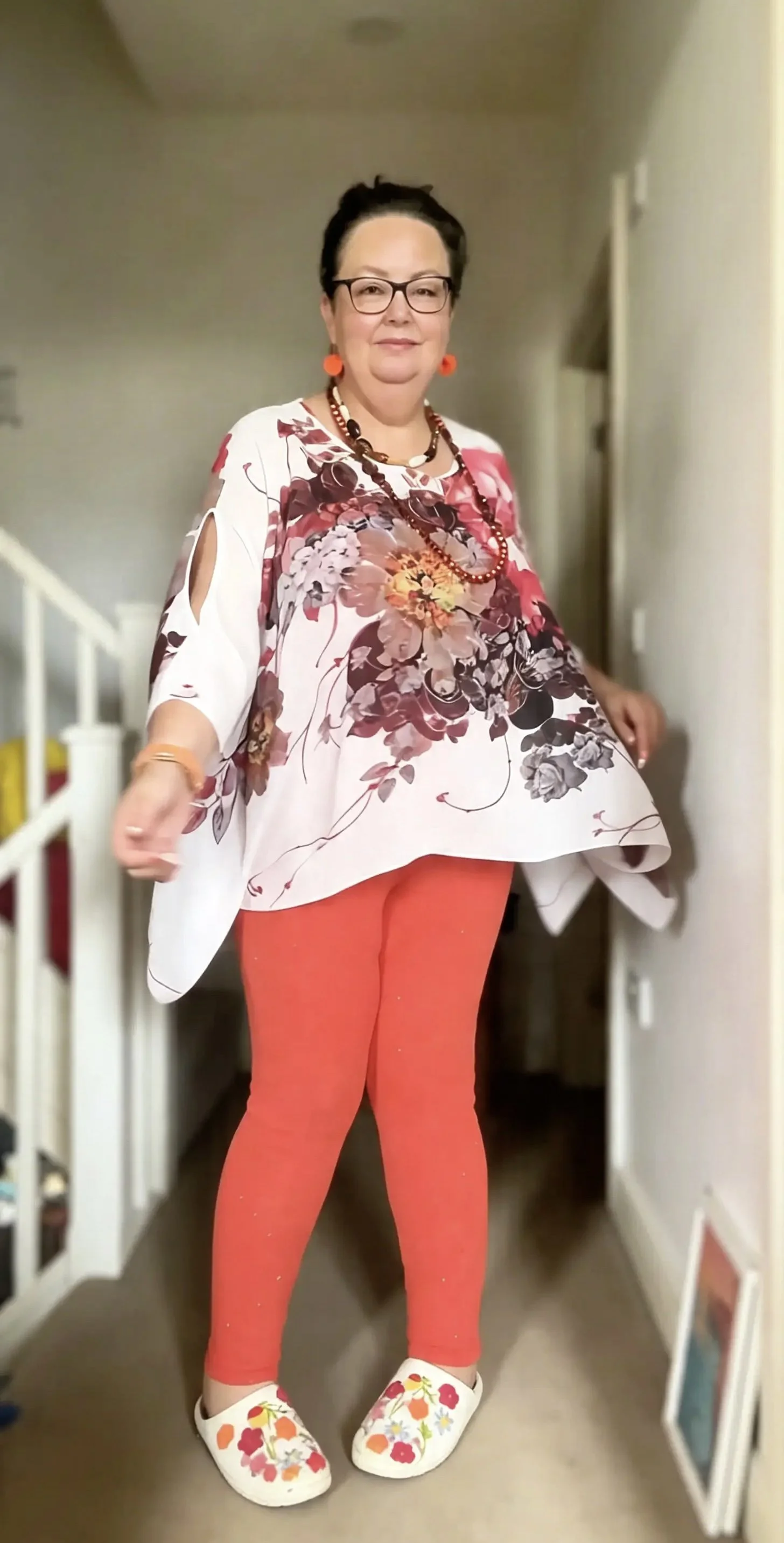Allison, looking happy with bright orange leggings and earrings by a staircase.