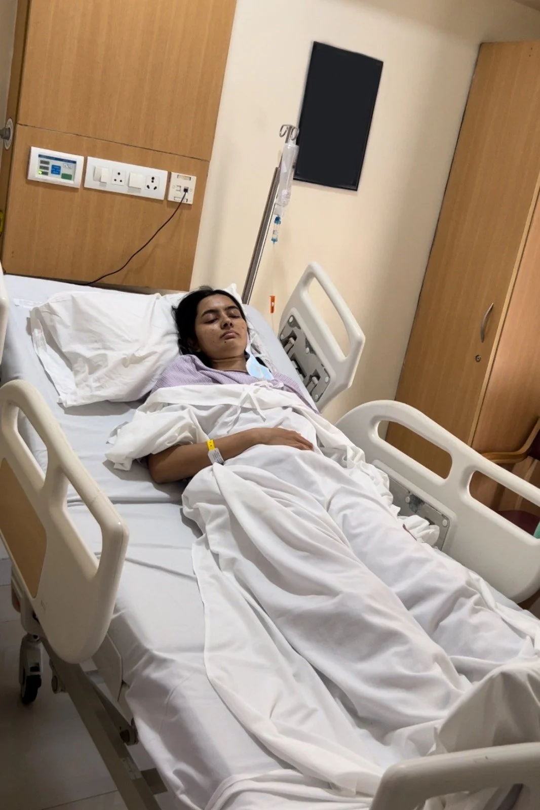 Rasika propped up in a hospital bed looking tired