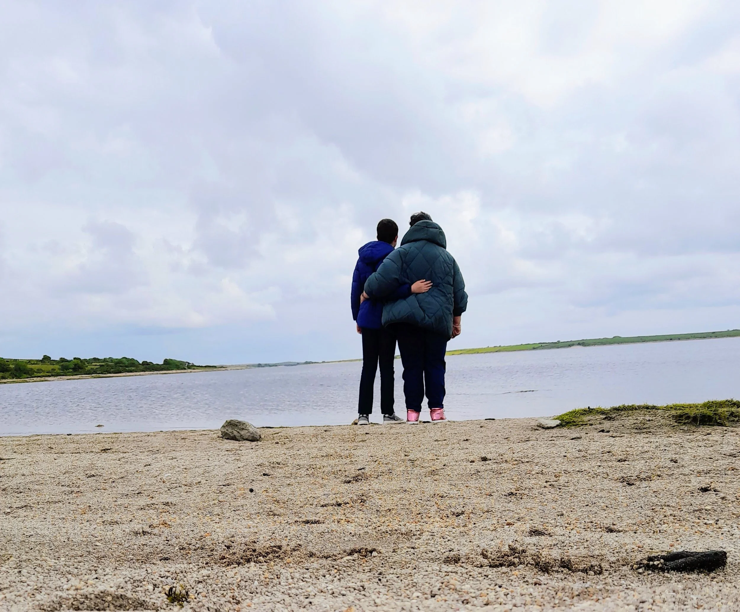 Allison and youngest son walking on a beach on a cold day with jackets - taking in some difficult news.