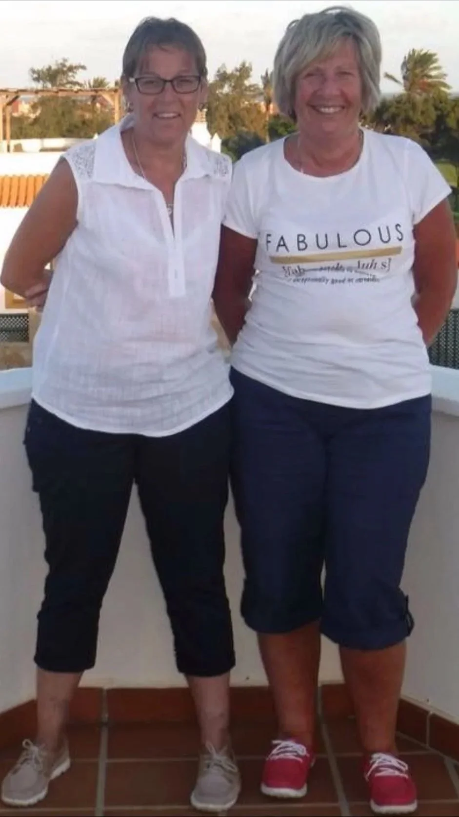 Julia and her best friend standing on a balcony with short sleeve shirts and big smiles