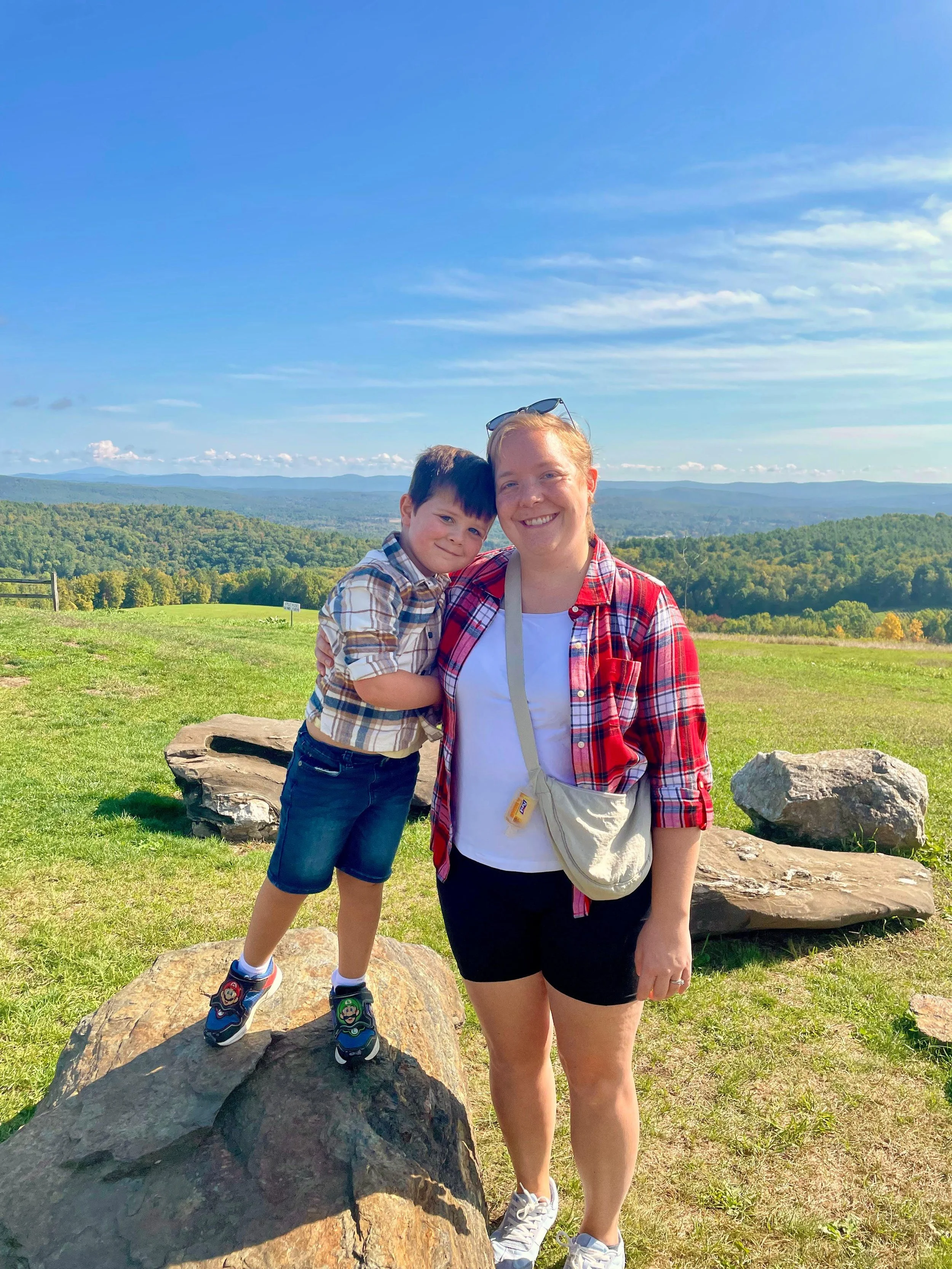 Loryn and son smiling big on a field with a big blue sky behind them.