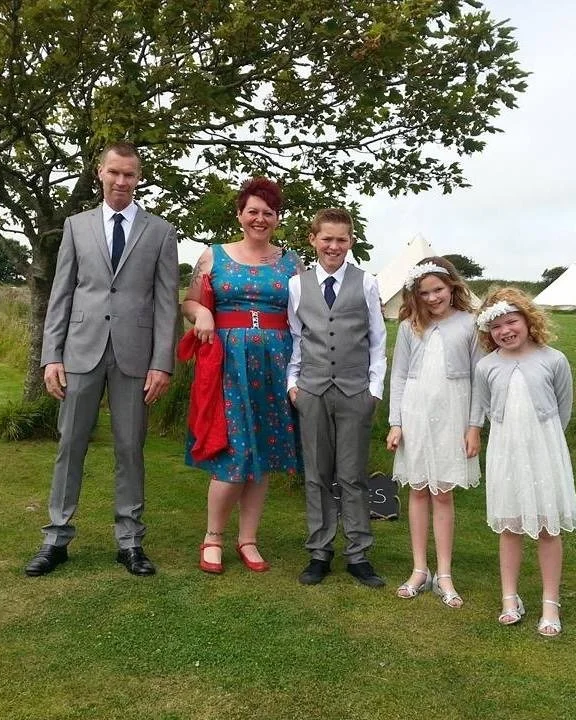 Julia and family all dressed up in suits and dresses. She stands with her husband by her side with her three young children by order of size (one son and two daughters)