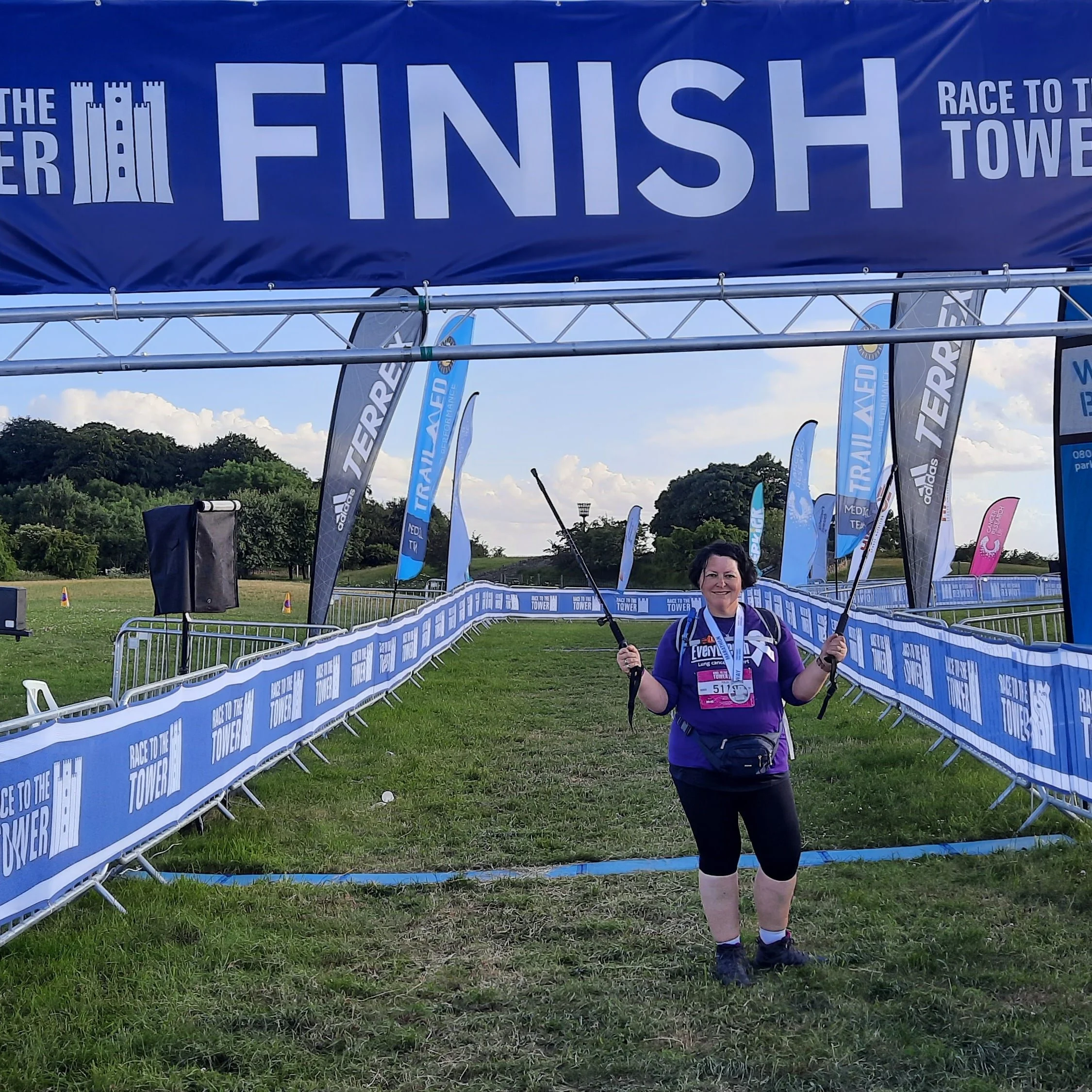 Julia, living with stage 4 lung cancer - seen crossing a finish line with walking sticks and a green lush field