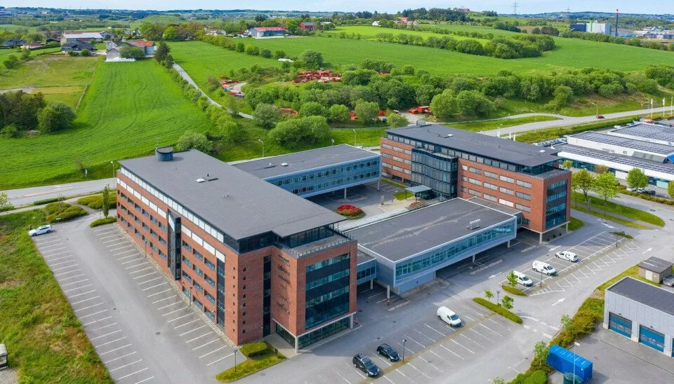 Et moderne kontorbygg med flere etasjer, omgitt av parkeringsplasser og grønne områder.