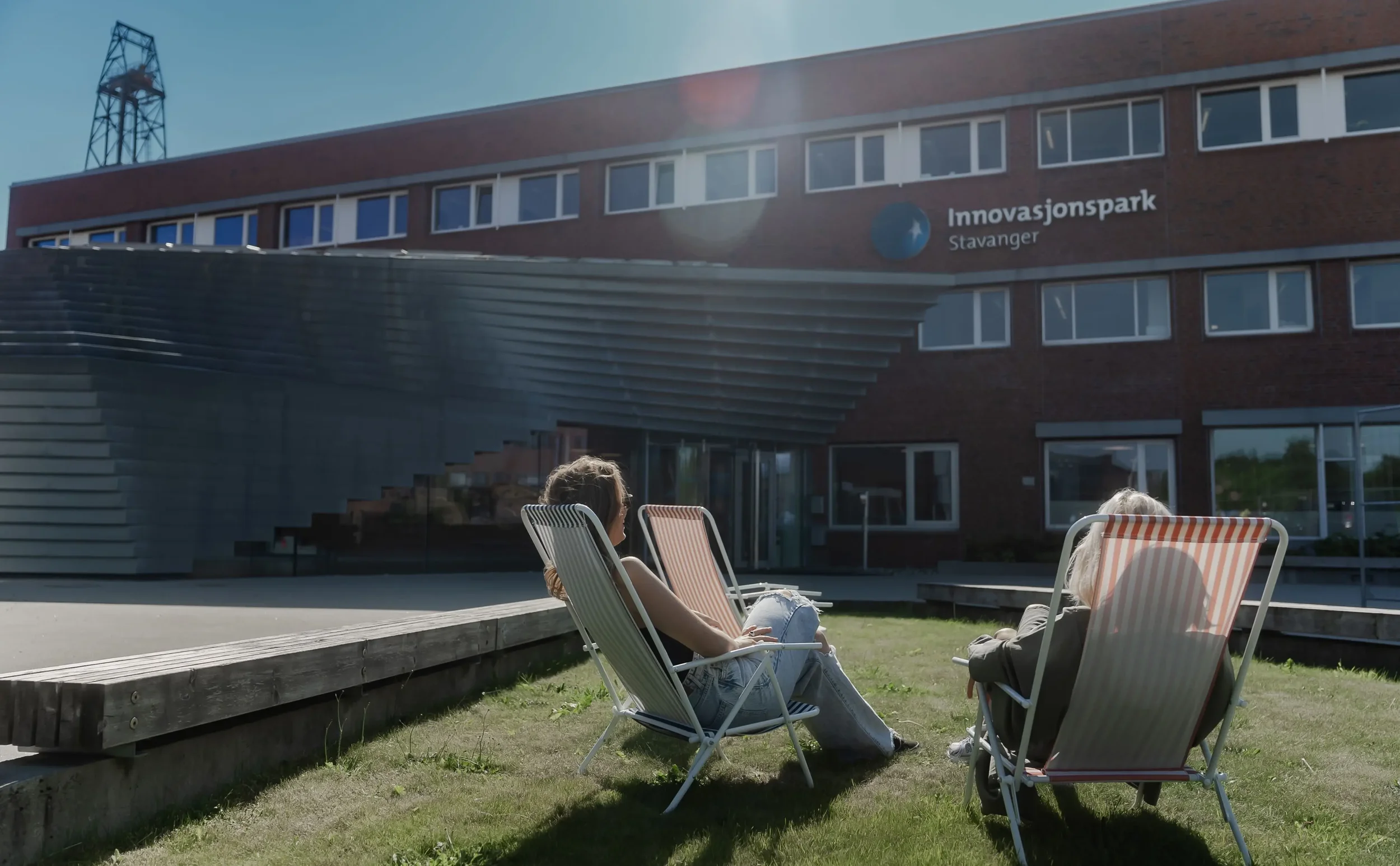To personer sitter i uteområder foran en bygning med skiltet «Innovasjonspark Stavanger».