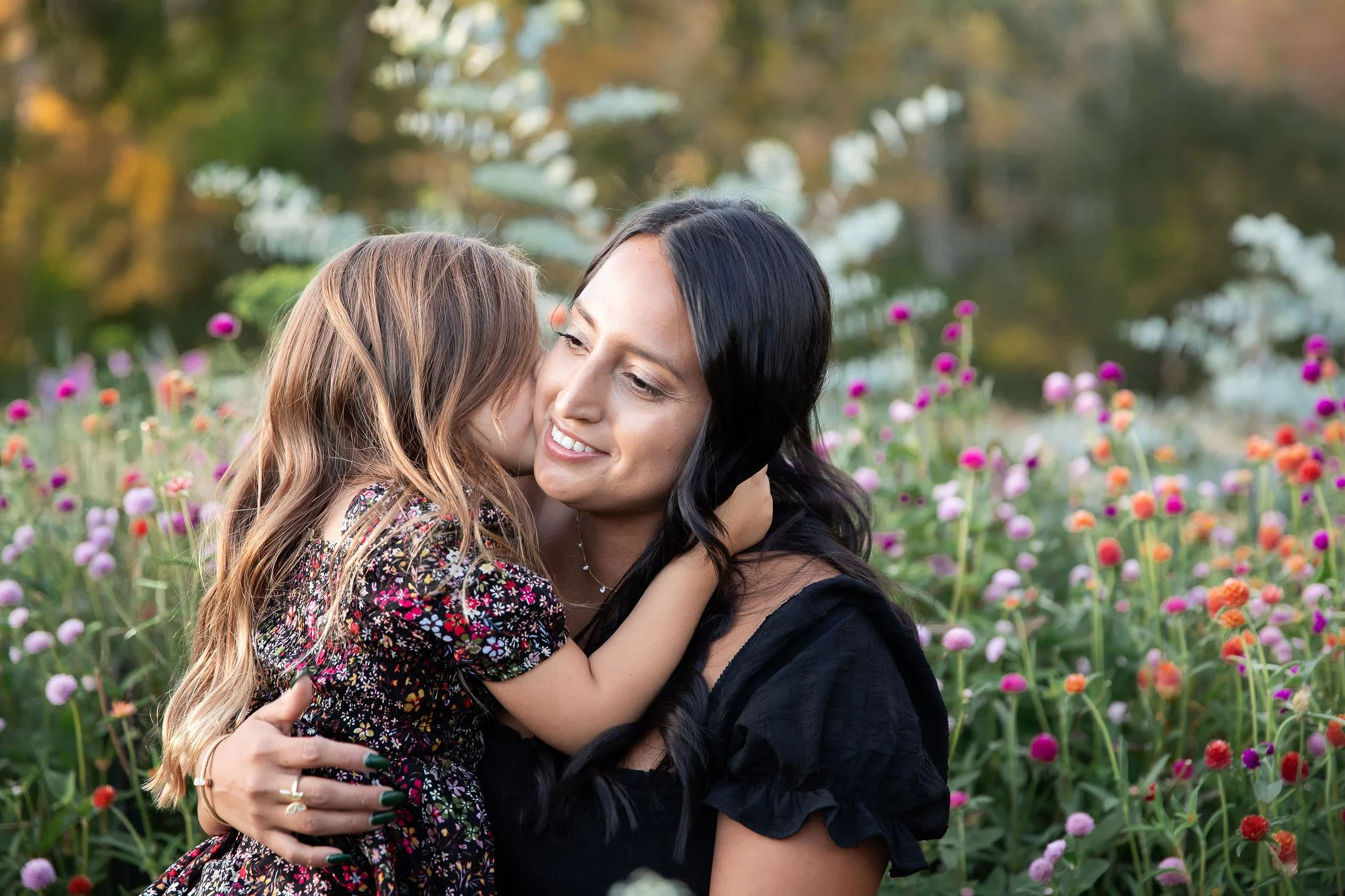Daughter giving her mom a sweet kiss at a family photo session during golden hour at the flower farm