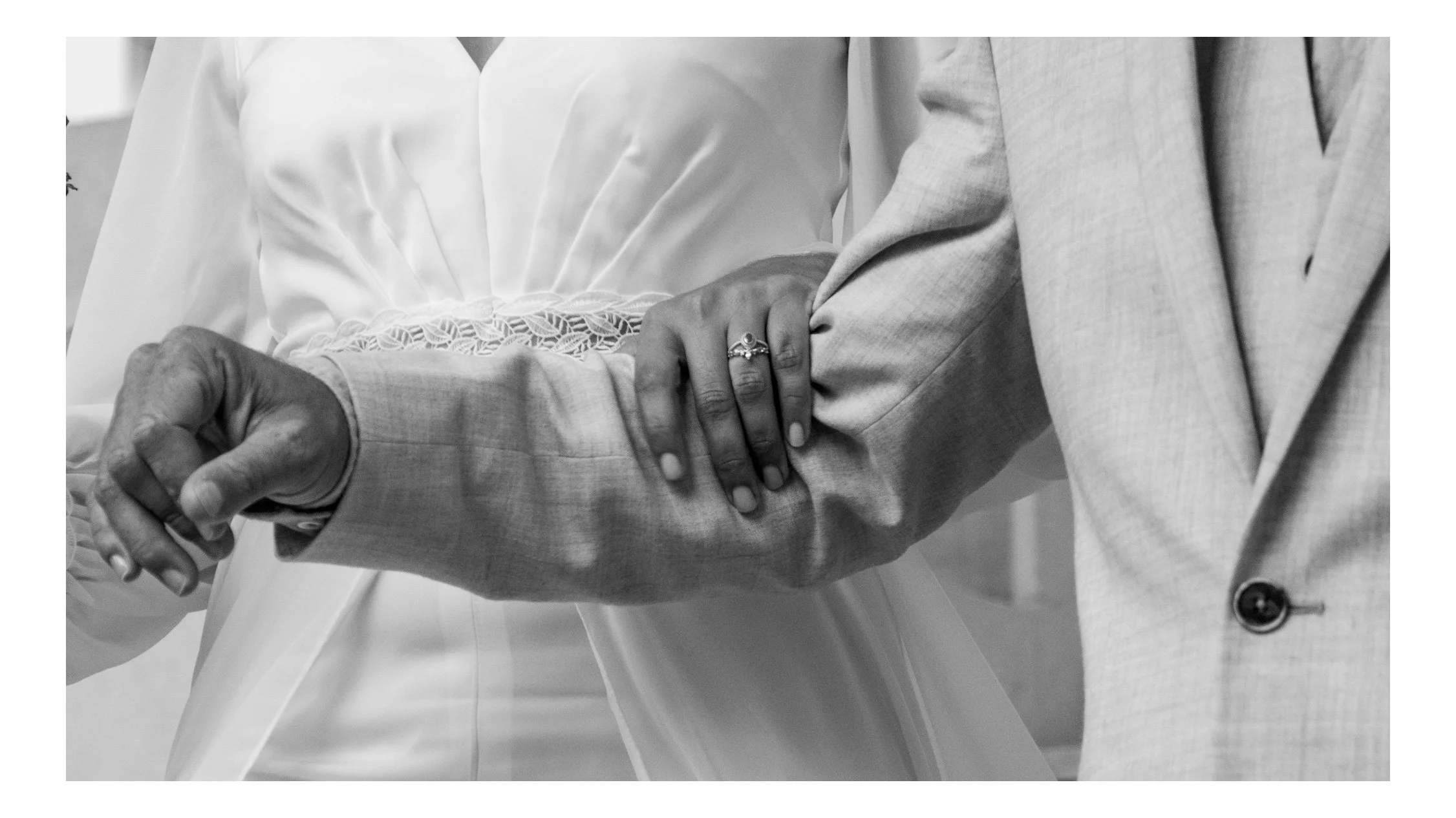 Un couple tenant la main lors d'une cérémonie de mariage, la femme portant une robe blanche et le homme en costume clair.