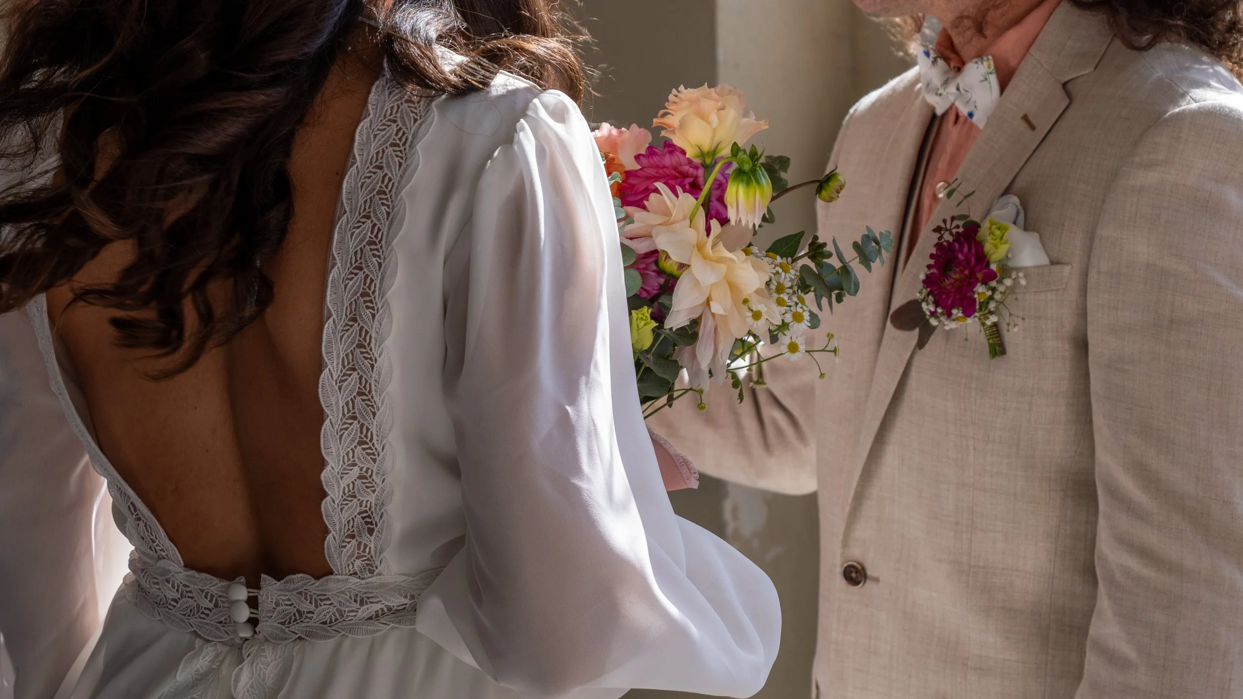 Une mariée portant une robe blanche avec des détails en dentelle, recevant un bouquet de fleurs colorées, lors d'une cérémonie de mariage.