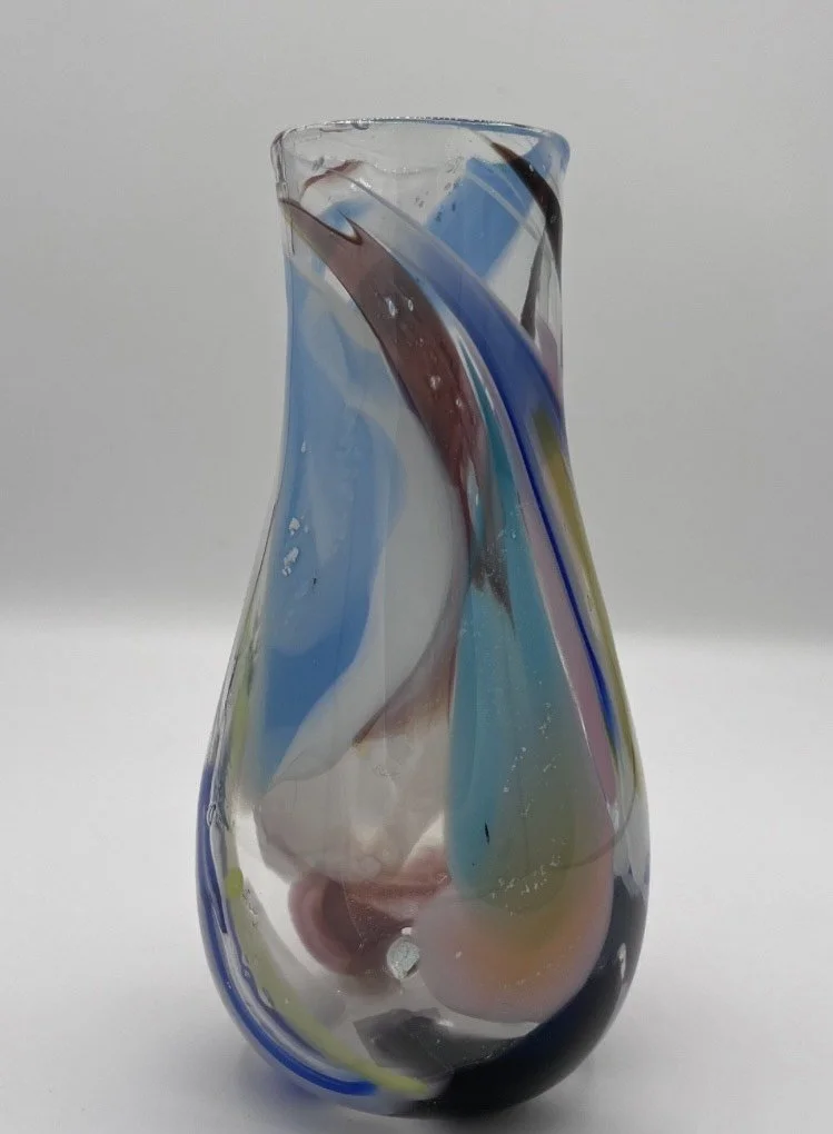 Colorful, abstract glass vase with swirls of blue, brown, pink, and yellow on a white background.