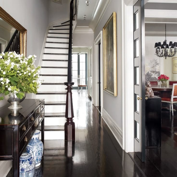 Elegant hallway with dark wood floors, a staircase, decorative console table with flowers, and vases.