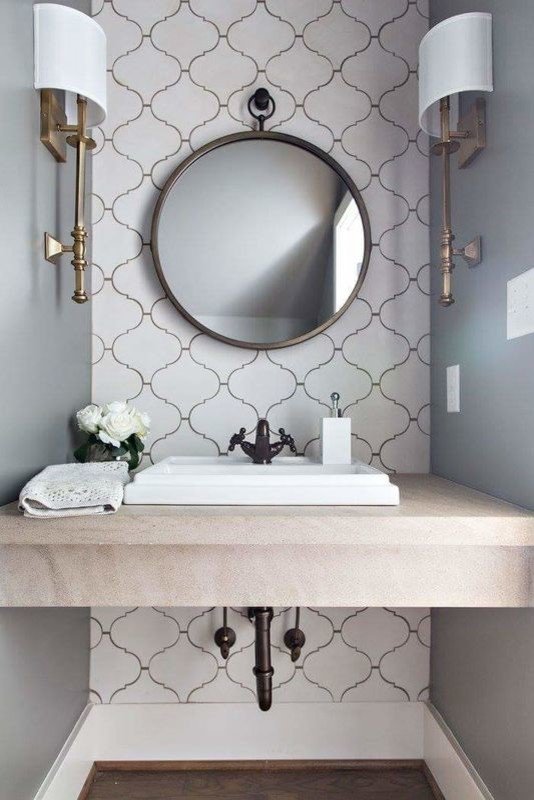 Small bathroom vanity with a round mirror, patterned wallpaper, sconces, and a white sink.