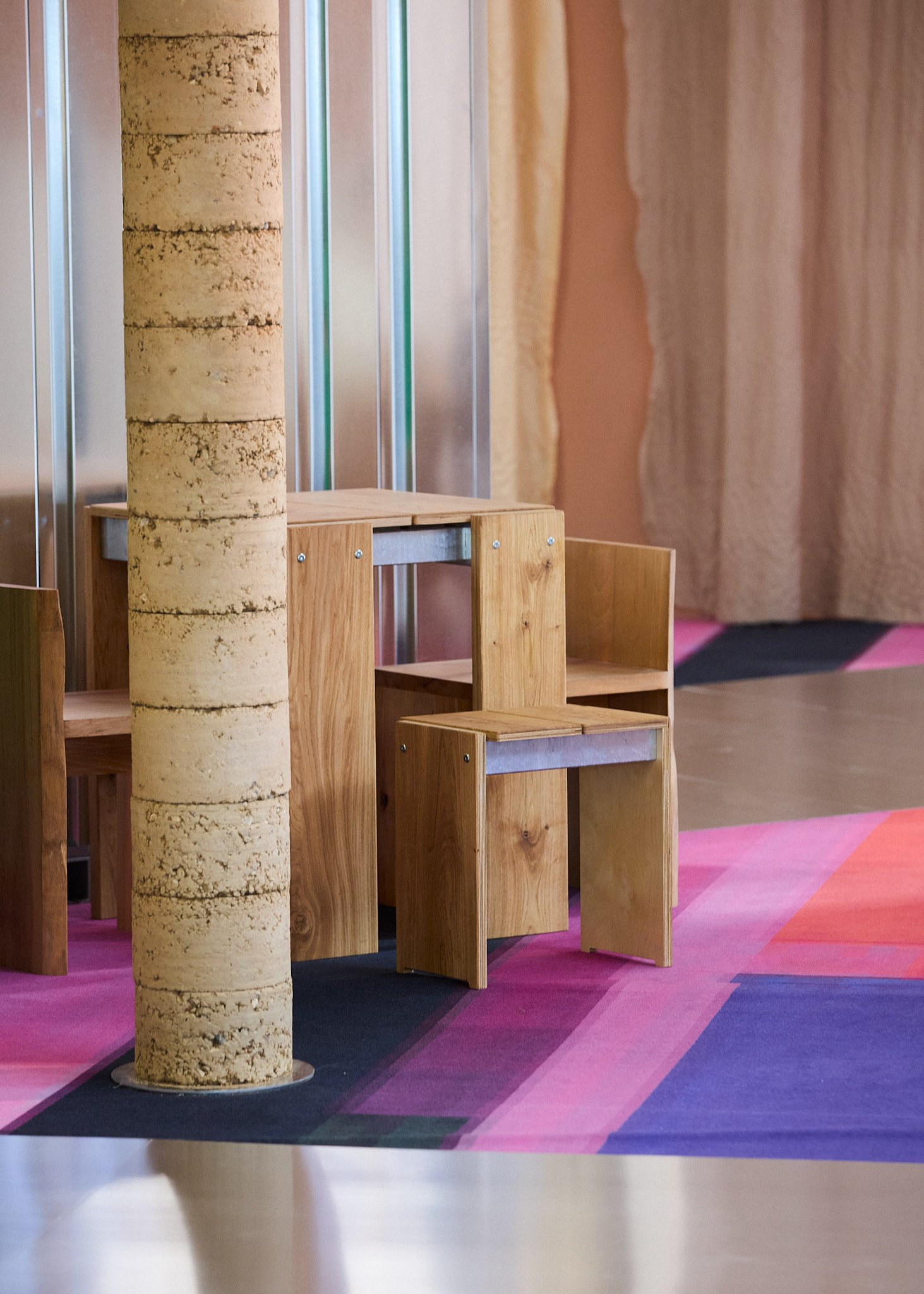 Small wooden furniture pieces, including chairs and a table, arranged indoors with a colorful carpet and a round tree trunk in the background.