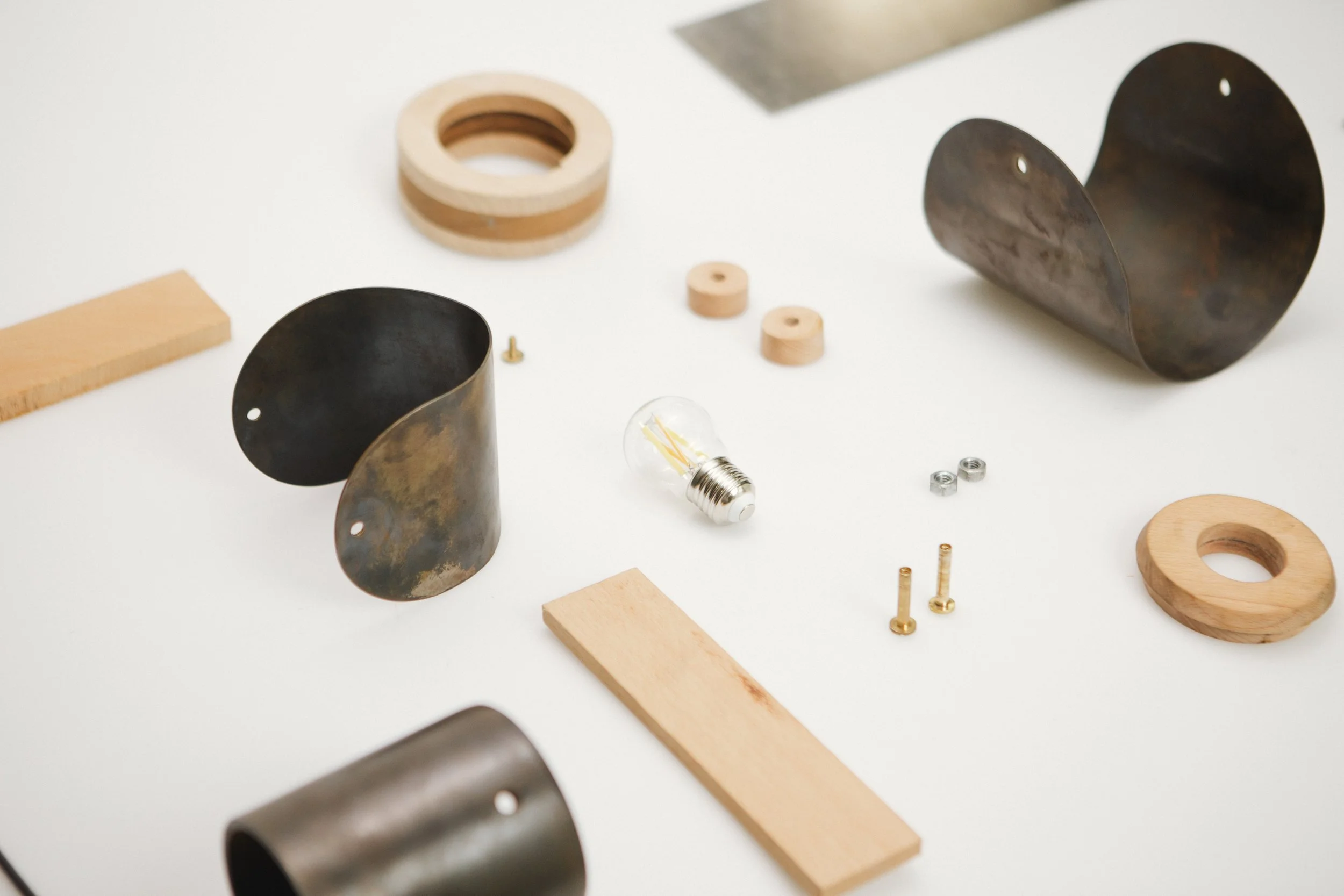 Disassembled light fixture parts including black metal shades, wooden rings, screws, a light bulb, and other hardware laid out on a white surface.