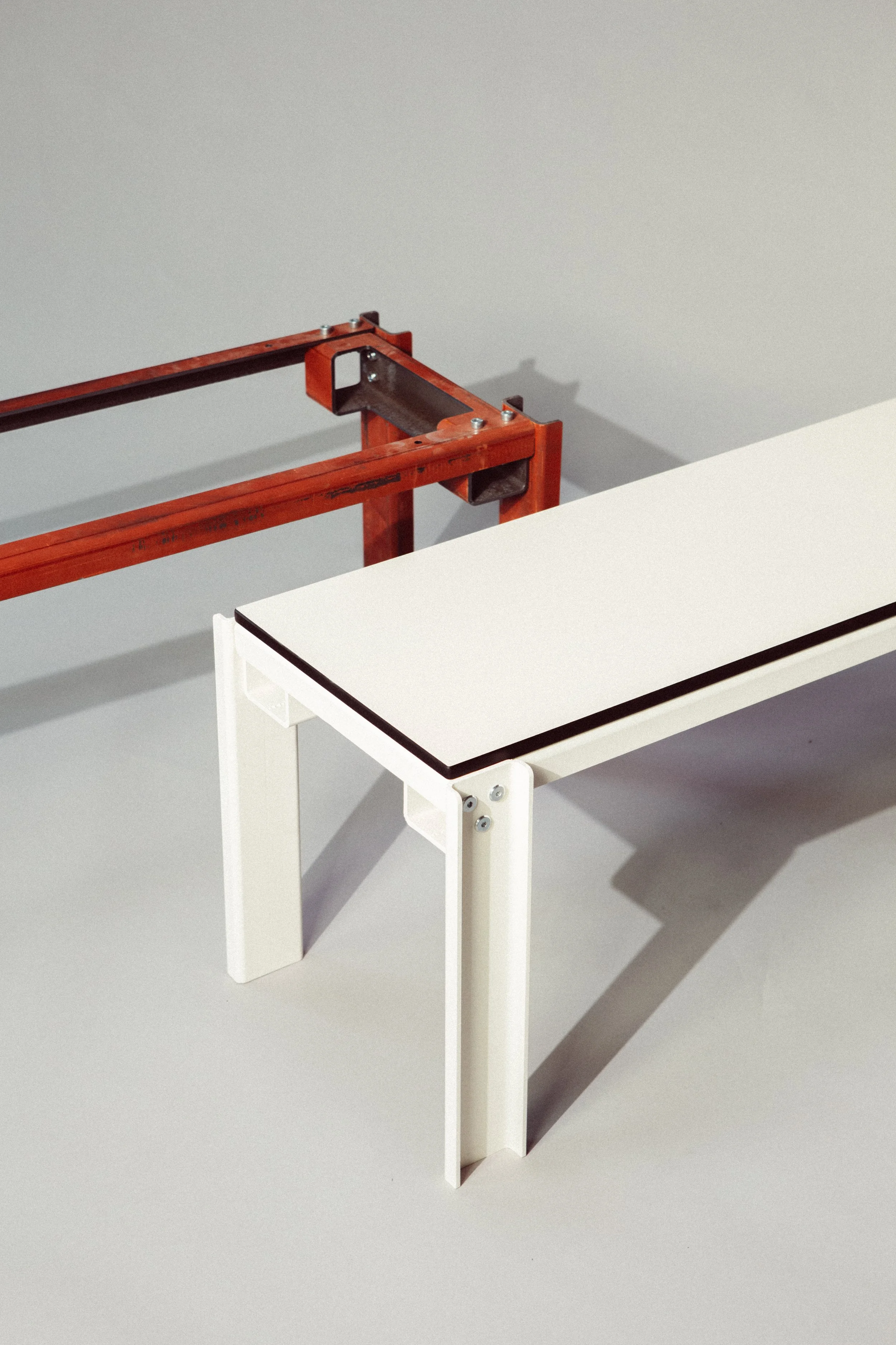 A white table with metal legs next to a red metal frame on a light gray background.