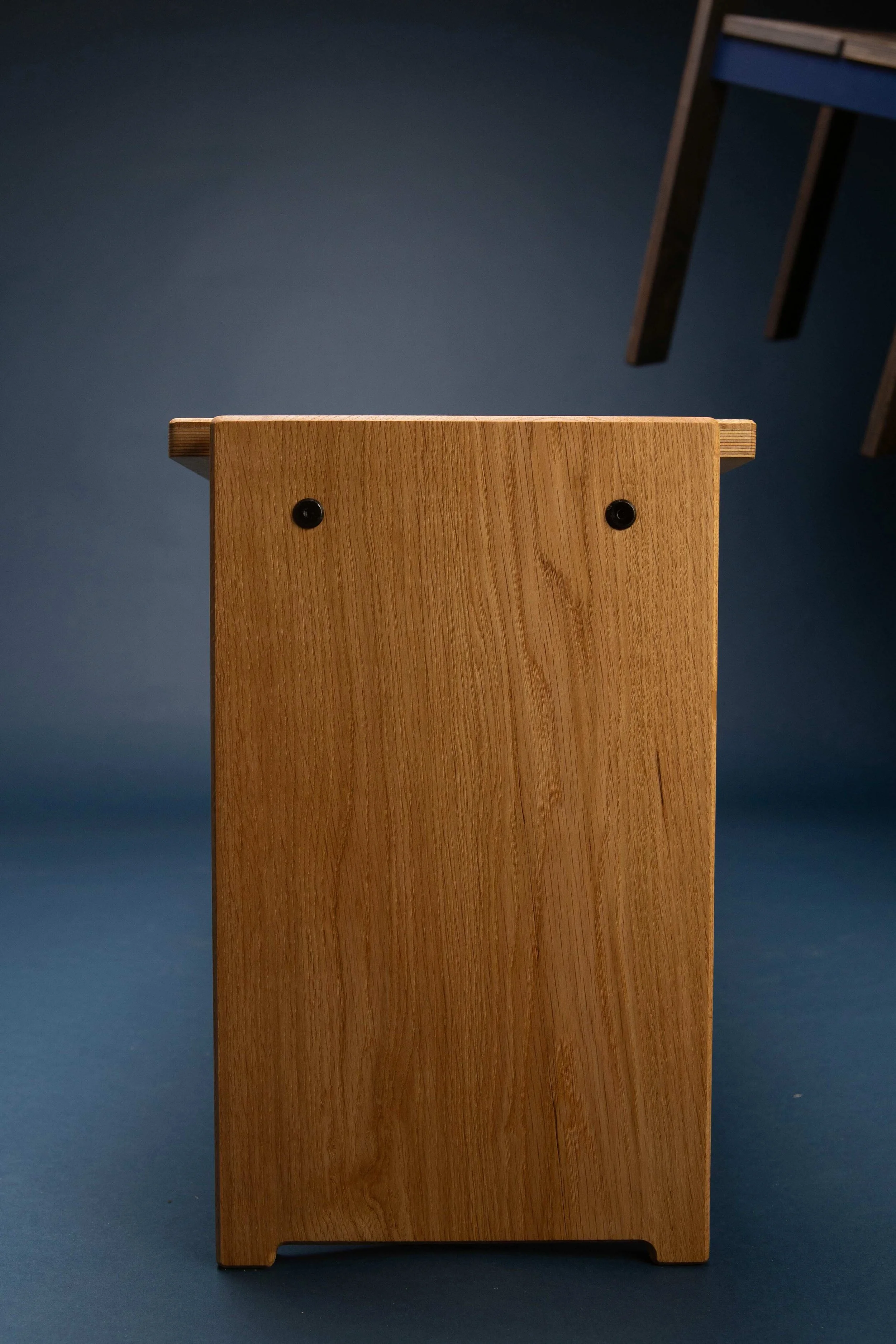A wooden stool viewed from the back, showing two black screws and a blue floor in the background.