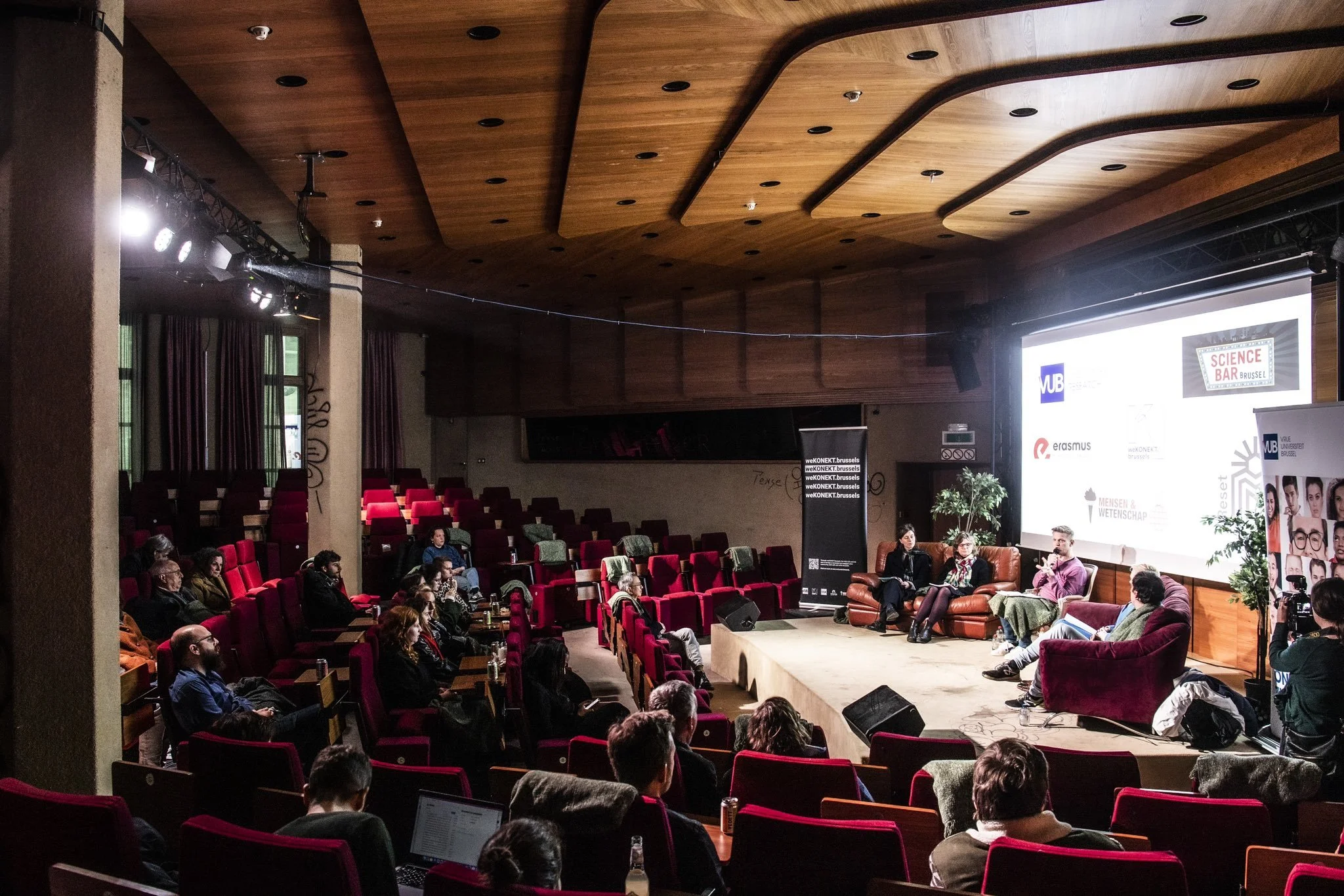 Panel discussion at a conference with five speakers on stage and audience seated in an auditorium.