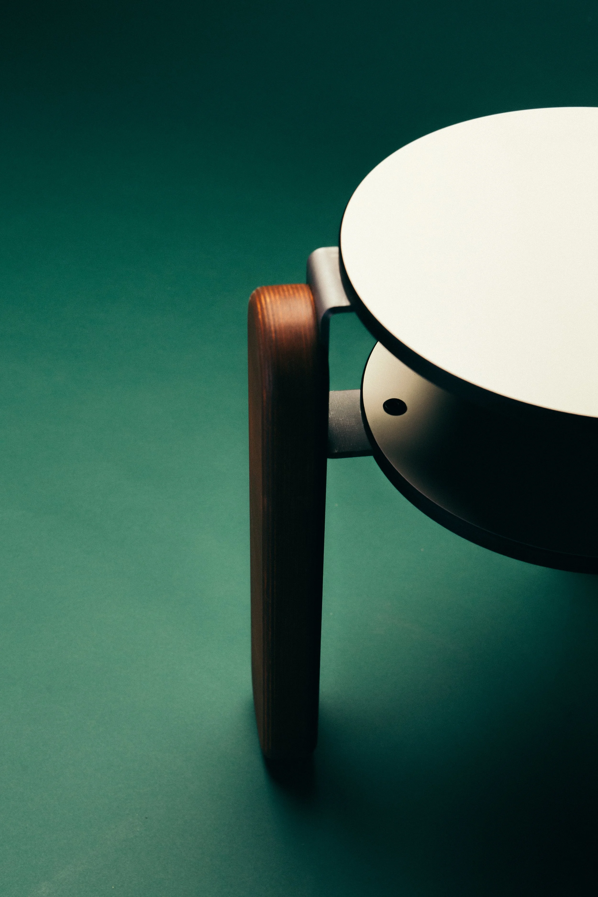 Close-up of a modern, minimalist coffee table with a round white top and wooden legs against a dark green background.