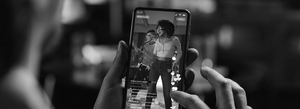 A person holding a smartphone recording a video of two women dancing indoors.
