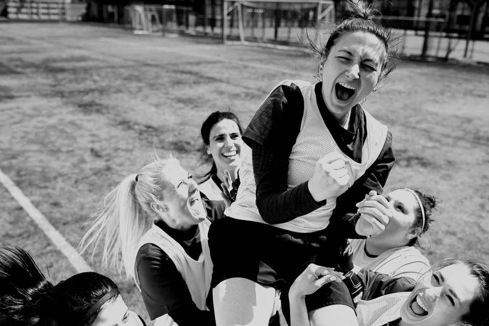 Group of women celebrating on a sports field, lifting one woman in excitement.