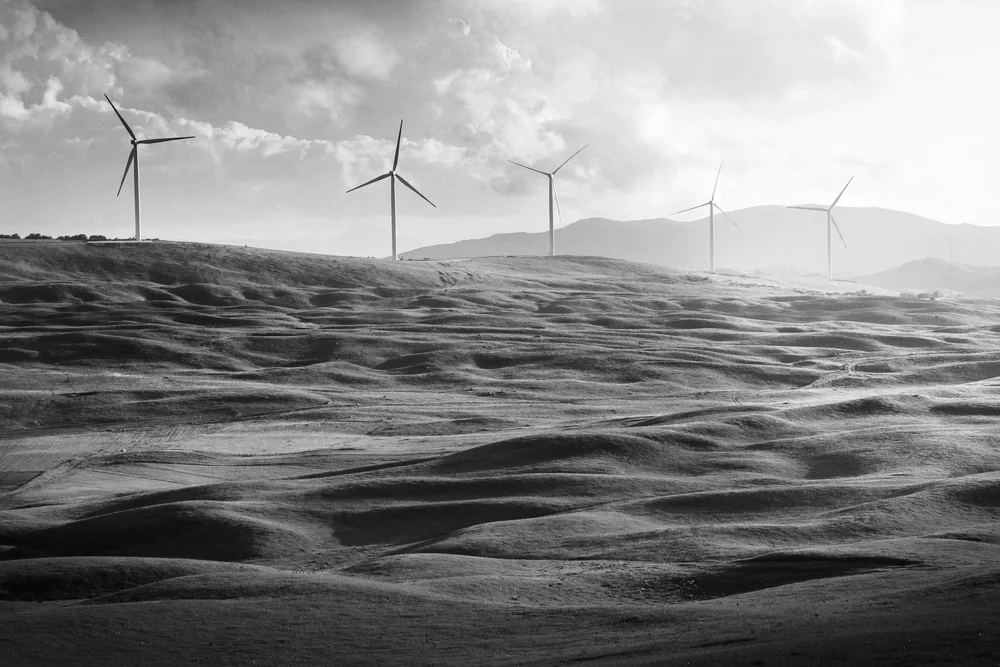 Landscape of wind turbines on rolling hills with mountains in the background, black and white photo.