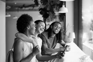Three friends sitting together at a counter in a coffee shop, enjoying conversation and laughter.