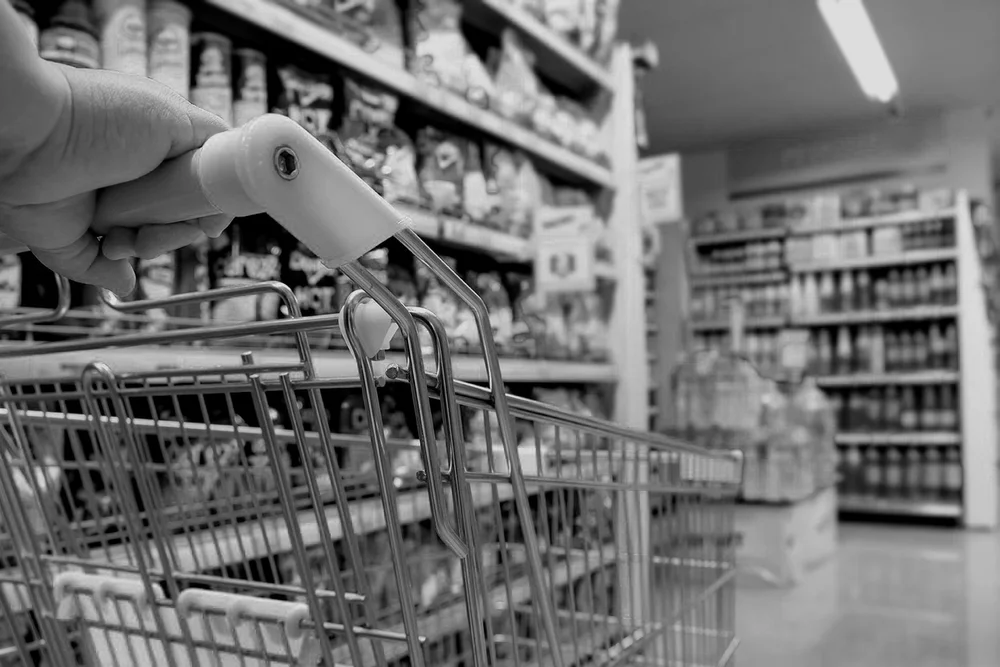 A person pushing a shopping cart in a grocery store aisle with shelves stocked with various products.