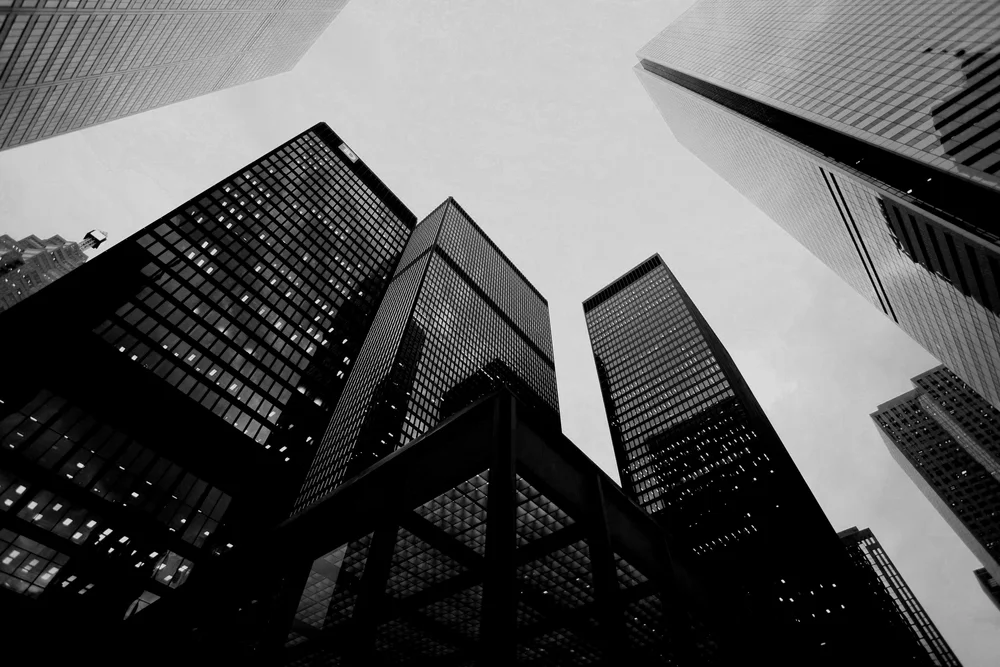 Black and white photo of tall skyscrapers in a city viewed from the ground looking up.