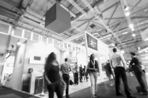 People walking and standing around exhibition booths at a convention center with hanging signs.