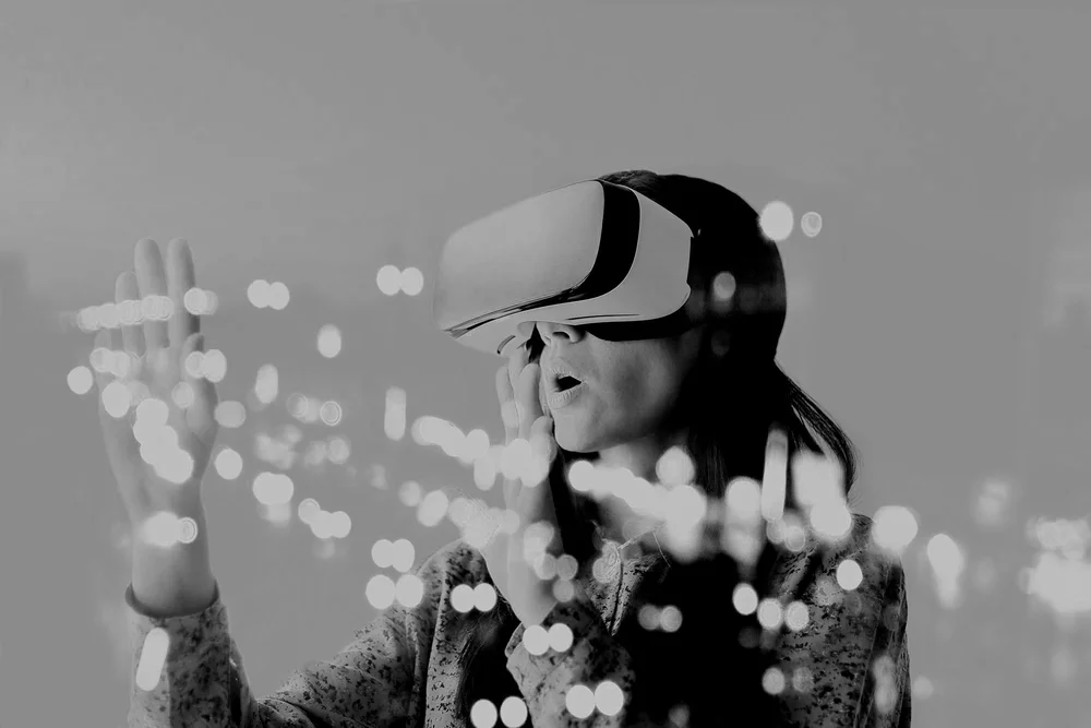 A woman using a virtual reality headset, touching a transparent surface with her right hand, with blurred city lights in the background.