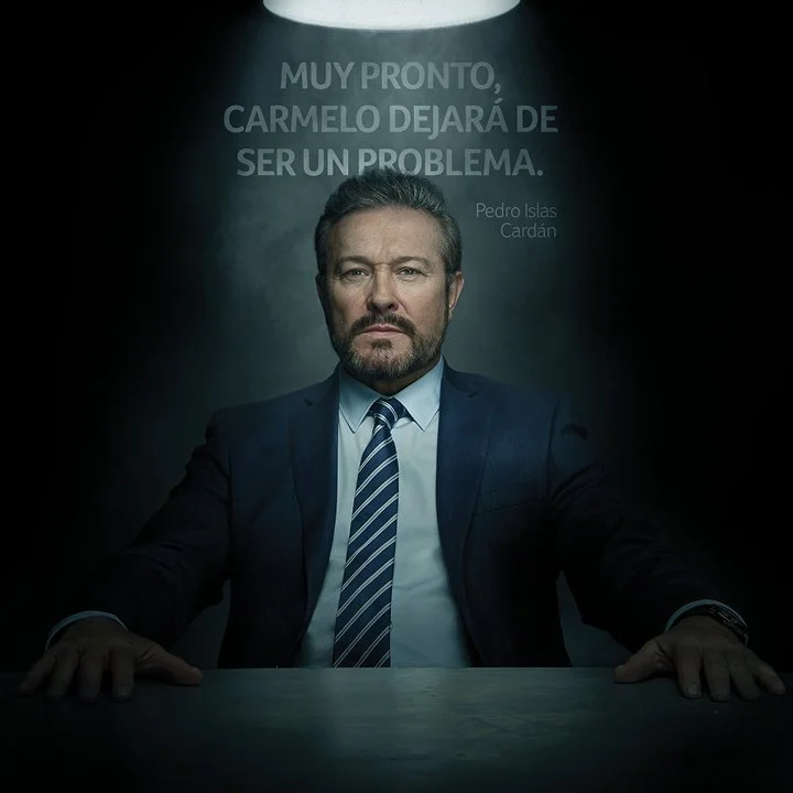 A man in a suit and tie sitting at a table with a serious expression, illuminated by a spotlight, with a quote in Spanish above his head.