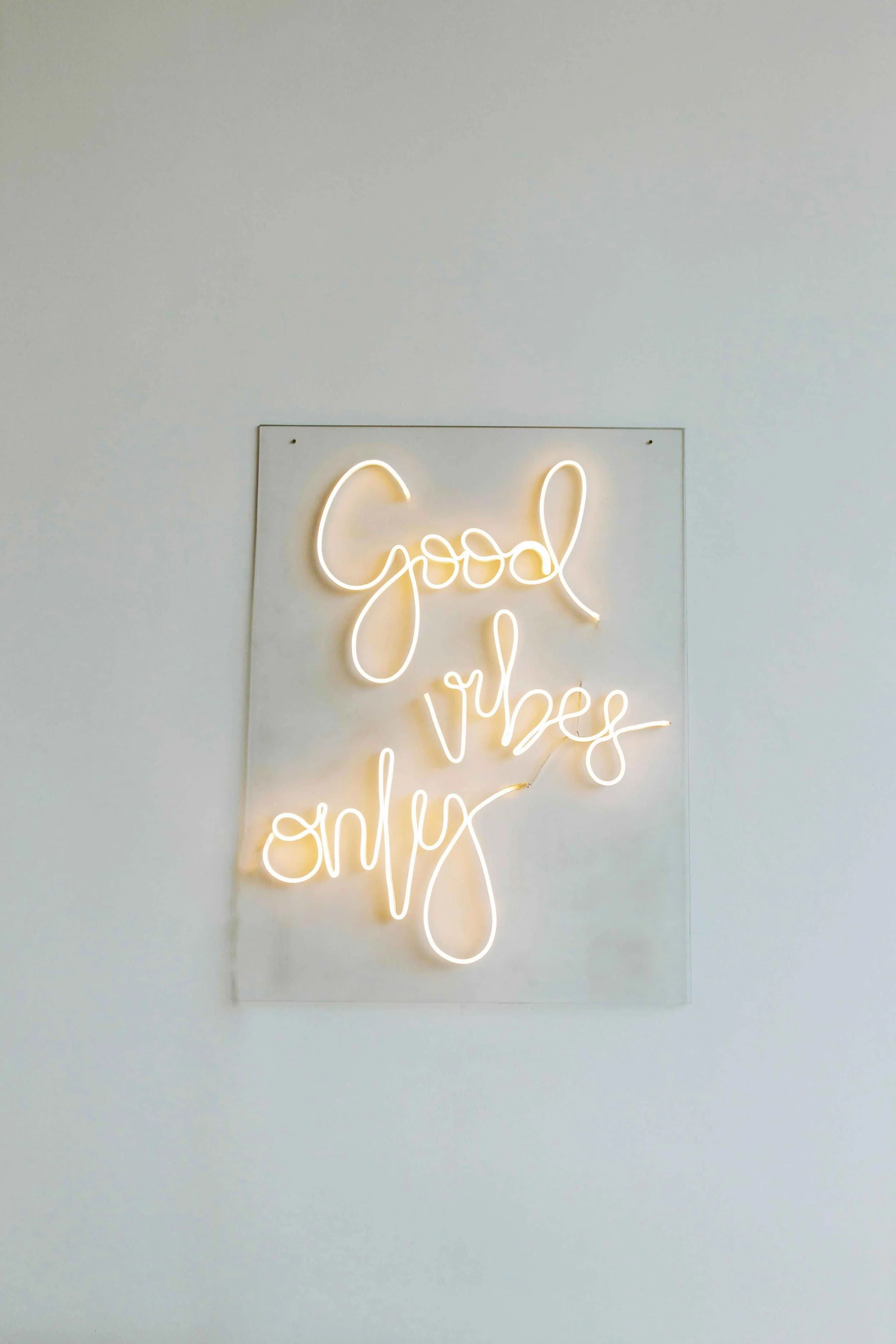 Neon sign with the phrase 'Good vibes only' in cursive script on a white wall.