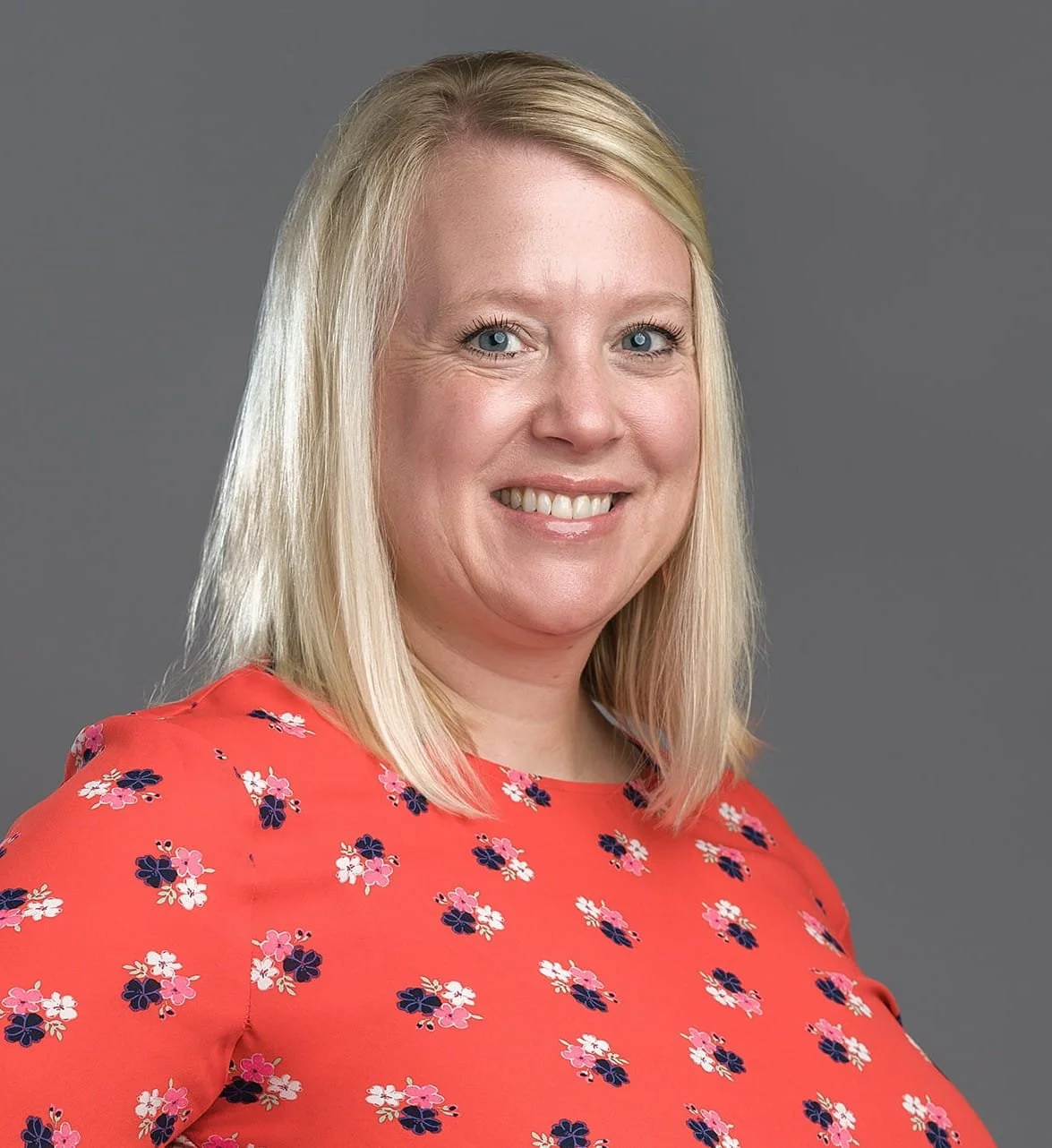 Professional headshot of a man with glasses, wearing a suit and tie, against a dark teal background.