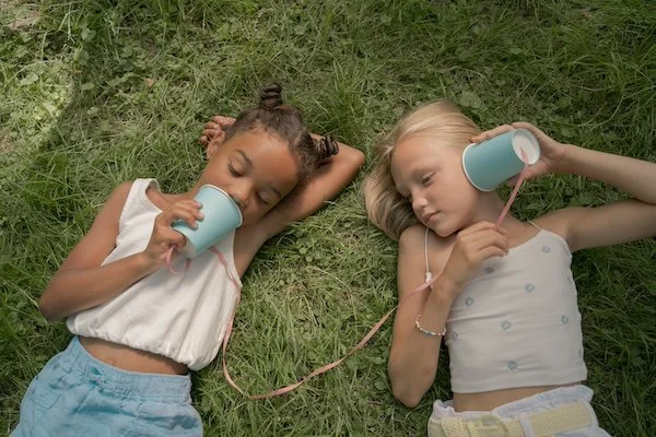 Two children using a cup and string telephone, illustrating how to ask businesses for donations through simple, relationship-first communication.