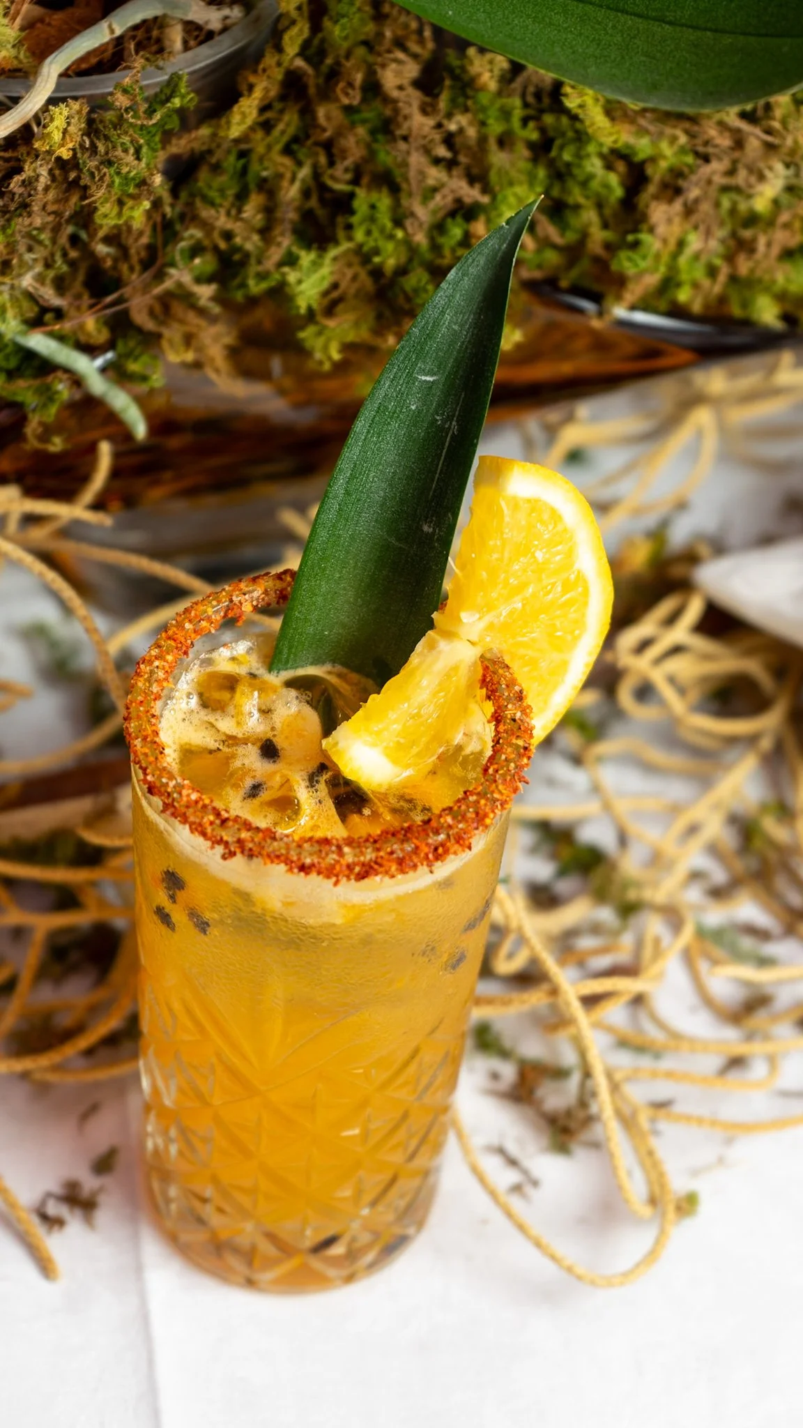 Cóctel de color amarillo con rodaja de naranja, piña y borde de chile en polvo.