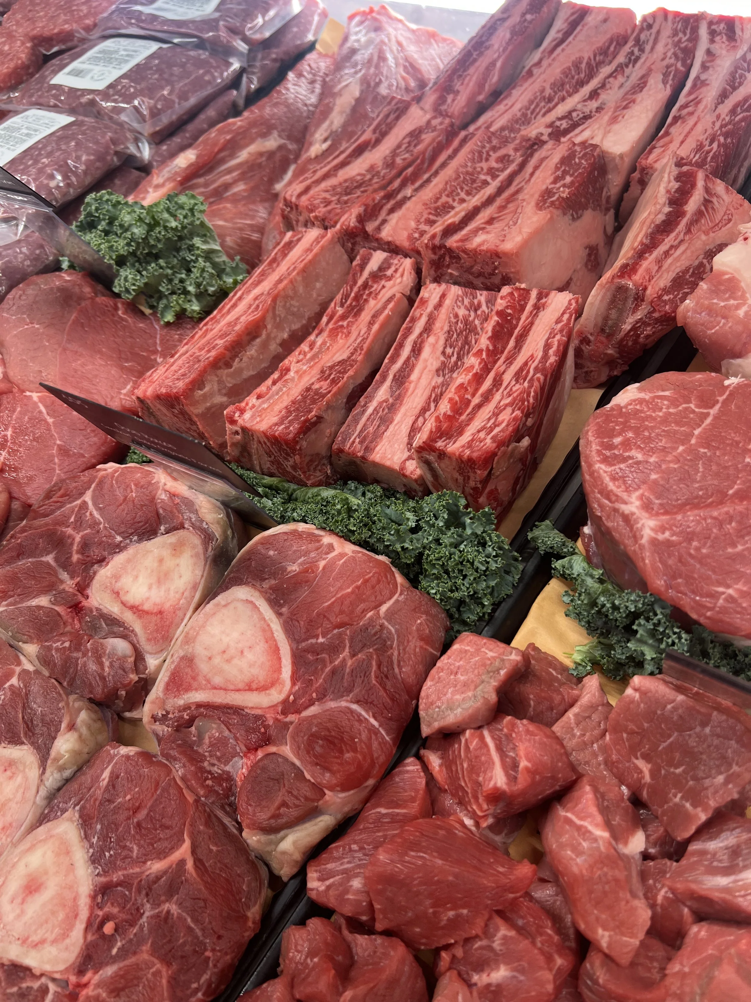 Assorted cuts of fresh red beef, including steaks and ribs, arranged on display with decorative green leafy garnish.